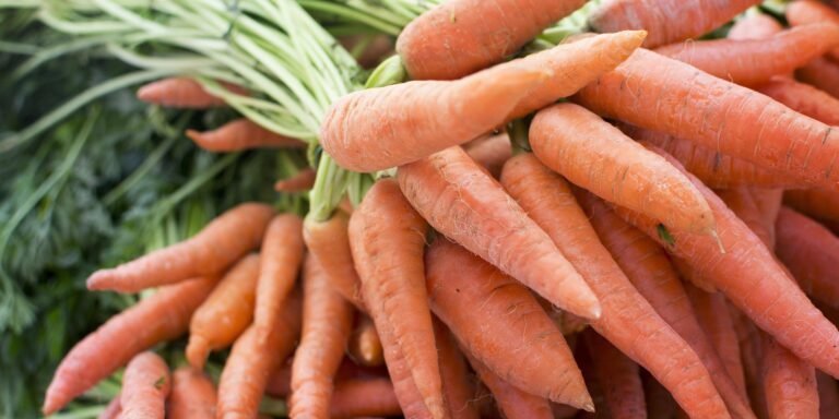 Close-up of vibrant orange carrots with green tops in a pile. The mood is fresh and natural, with no visible text or actions.